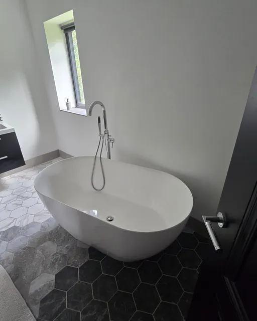 Freestanding bath beside a window, with dark hexagon floor tiles