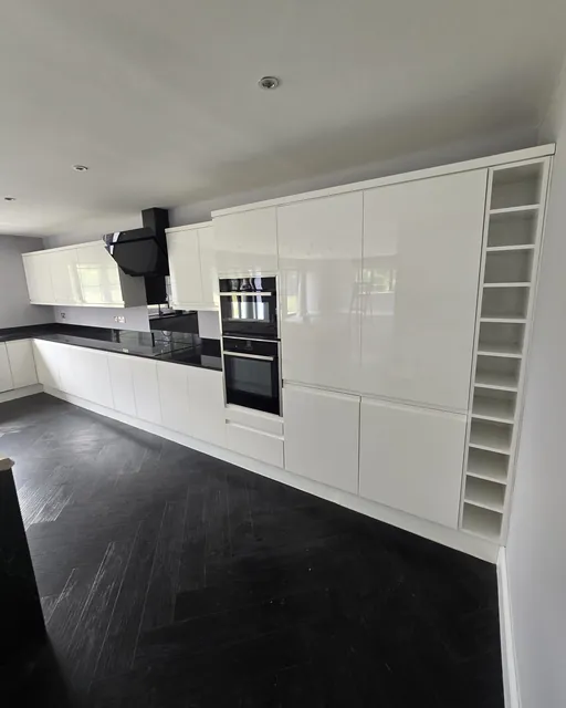Gloss white fitted kitchen with built-in ovens and dark slate-effect floor