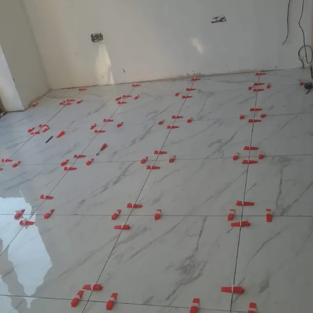 Marble-effect floor tiles being laid with levelling clips and spacers