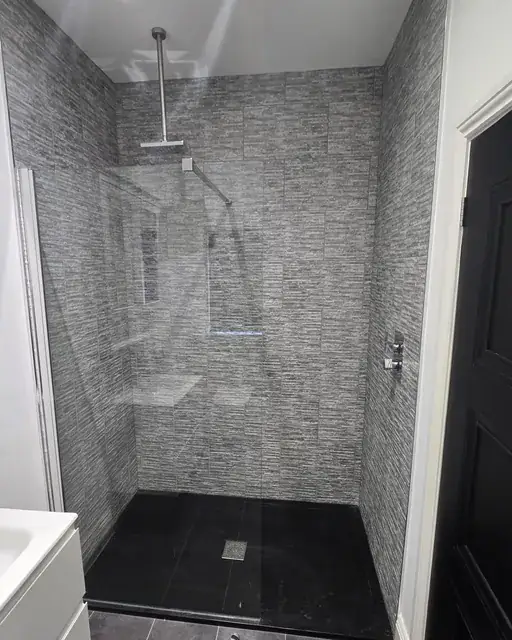 Walk-in shower room tiled in grey stone-effect tile with a black slate tray